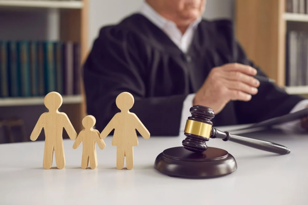 A judge with a gavel behind small wooden figures of a family
