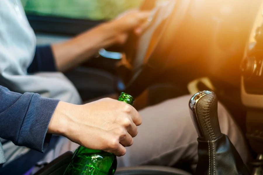 A driver holding a beer bottle while steering a car