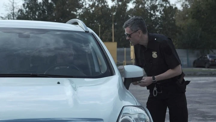 A police officer talking to the driver of a stopped white car