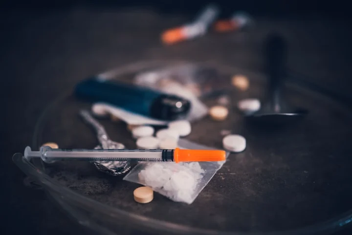 Pills, a syringe, a lighter and a bag of white powder on a dark table