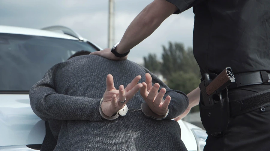 A police officer handcuffing a man against a white car