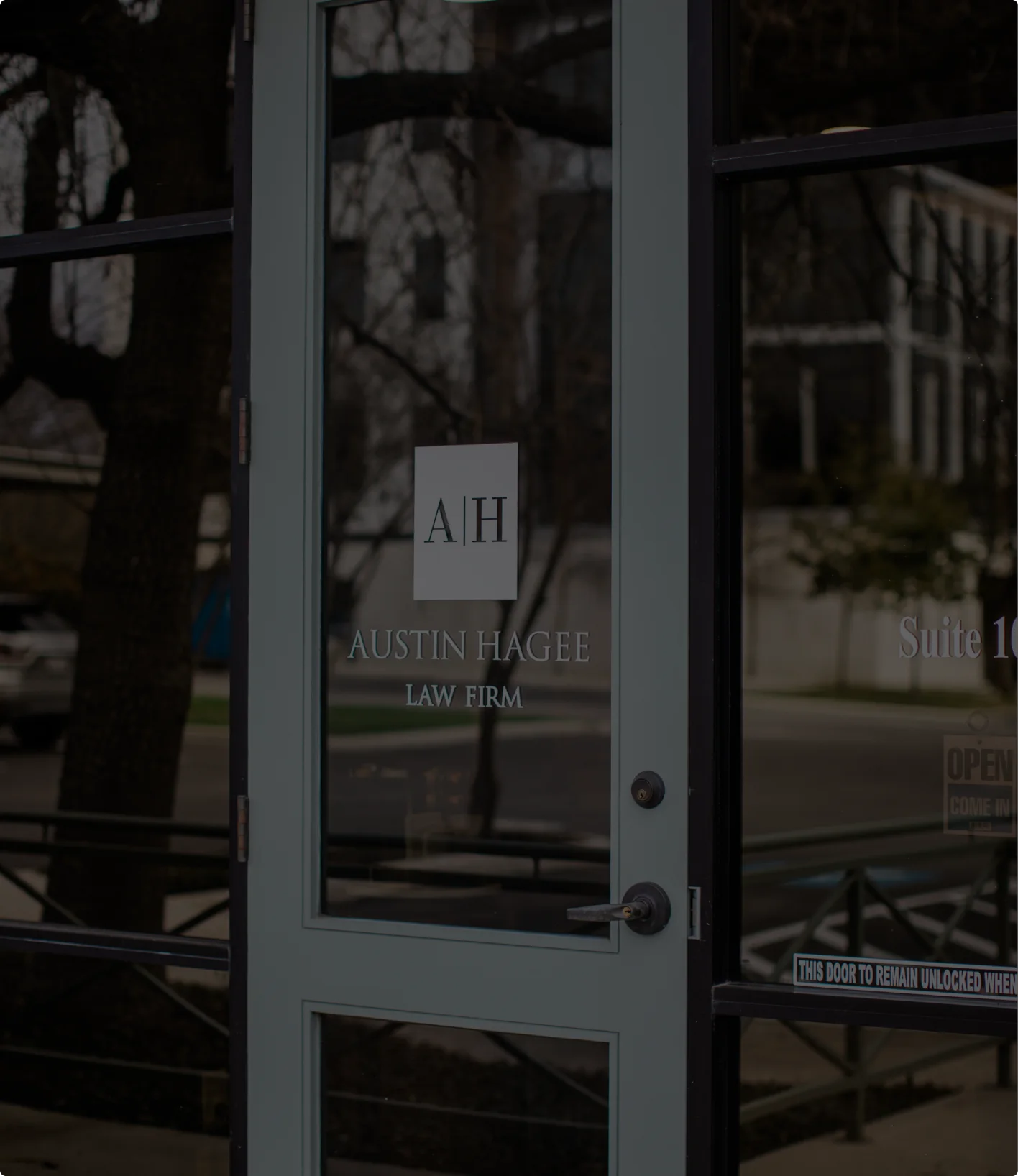 Glass office door etched with the A|H mark and the Austin Hagee Law Firm name, seen from the sidewalk